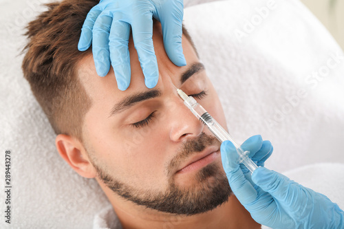 Handsome man receiving filler injection in beauty salon photo