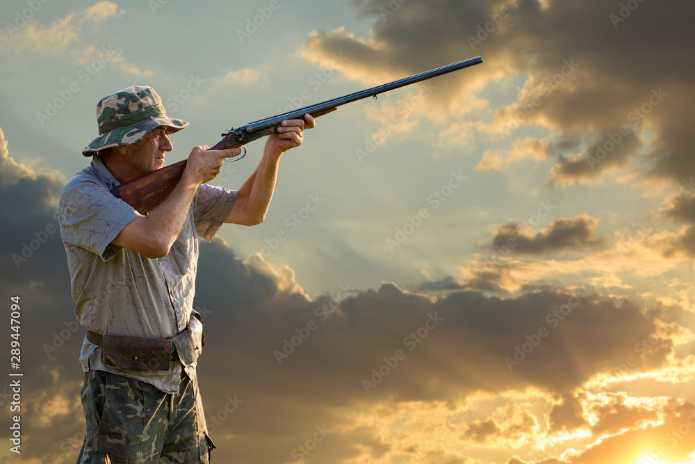 Hunting period, autumn season open. A hunter with a gun in his hands in hunting clothes in the autumn forest in search of a trophy. A man stands with weapons and hunting dogs tracking down the game. Hunting period, autumn season open. A hunter with a gun in his hands in hunting clothes in the autumn forest in search of a trophy. A man stands with weapons and hunting dogs tracking down the game.