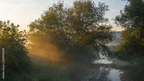 Dawn over the river, fog slowly rising from the water, its rays illuminate it