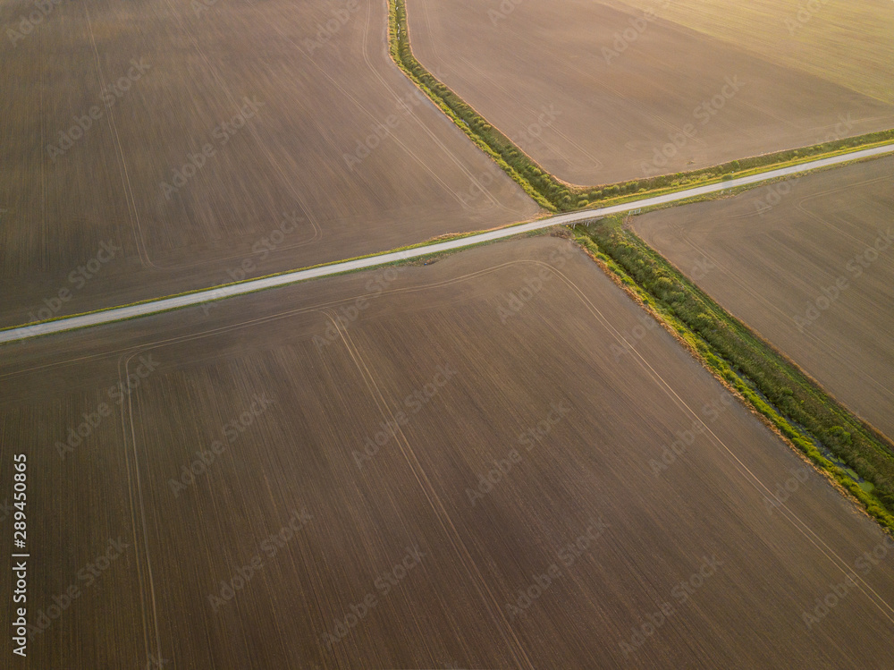 Aerial view of dirt road surrounded by ploughed agricultural fields during early fall sunset