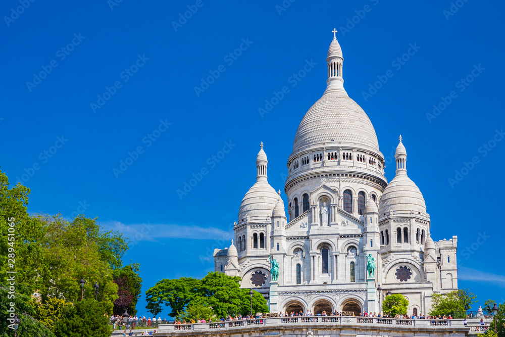 Basilica of the Sacré-Coeur, also known as the Sacred Heart, the famous church in Montmartre in Paris France on a summer day with a blue sky nestled on the hill surrounded 