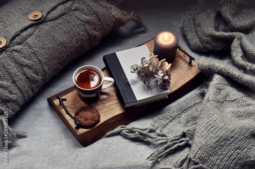 Cozy home with cup of tea with steam, blanket, book and candles. Hygge home interior