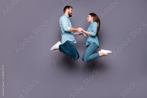 Full size photo of cheerful romantic students hold hand jump wear denim jeans isolated over grey background