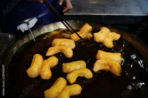 Chef making Youtiao in Hot Frying Pan in Local Market, Traditional Fried Dough Food. Chinese Cruller photo