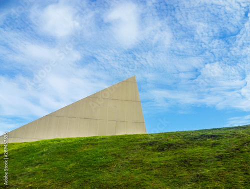 Photo of a triangular pyramid located on a hill, overgrown with green grass.