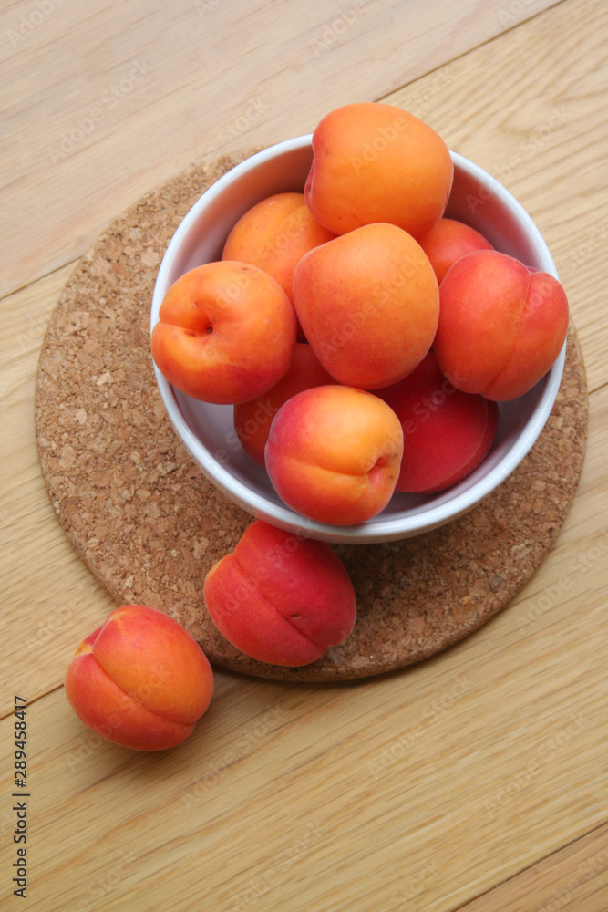 Fresh ripe apricots in a white bowl on wooden table. Prunus armeniaca fruits Fresh ripe apricots in a white bowl on wooden table. Prunus armeniaca fruits