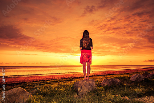 Frau mit rotem Rock geniesst den Sonnenuntergang am Meer
