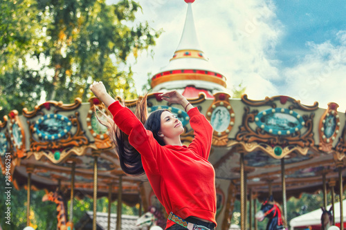 Young beautiful brunette woman happy in the Park on the background of bright colored carousel