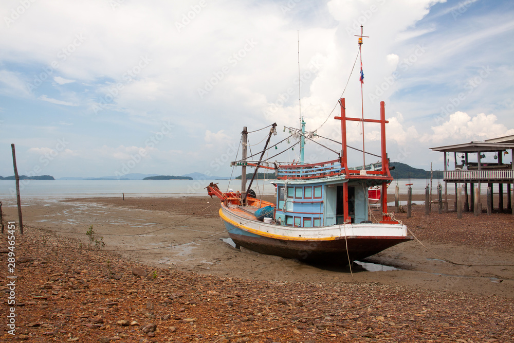 FIshing boat and wooden house at low tide beach, Koh Phangan island, Thailand.
