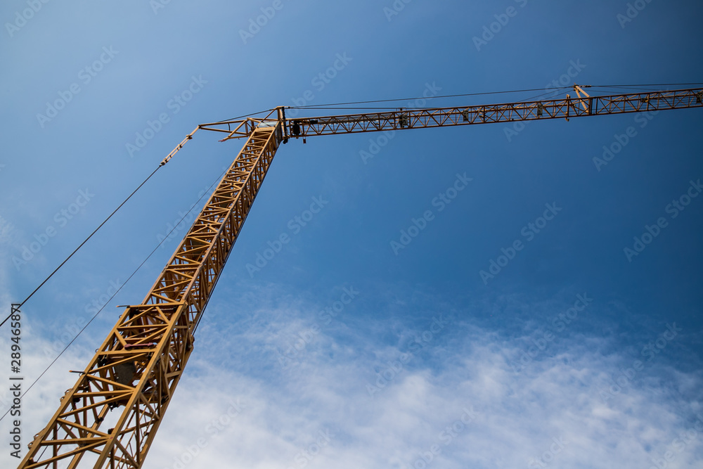 Construction site with cranes on sky background. Big yellow machinery construction crane tool of building industry for heavy lifting on blue sky background. Business engineering equipment modern