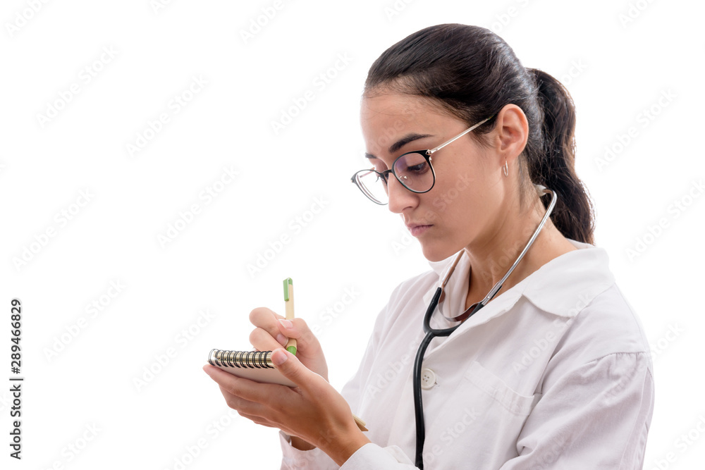 Caucasian young female doctor with glasses and stethoscope prescribing in a notebook on white background isolated