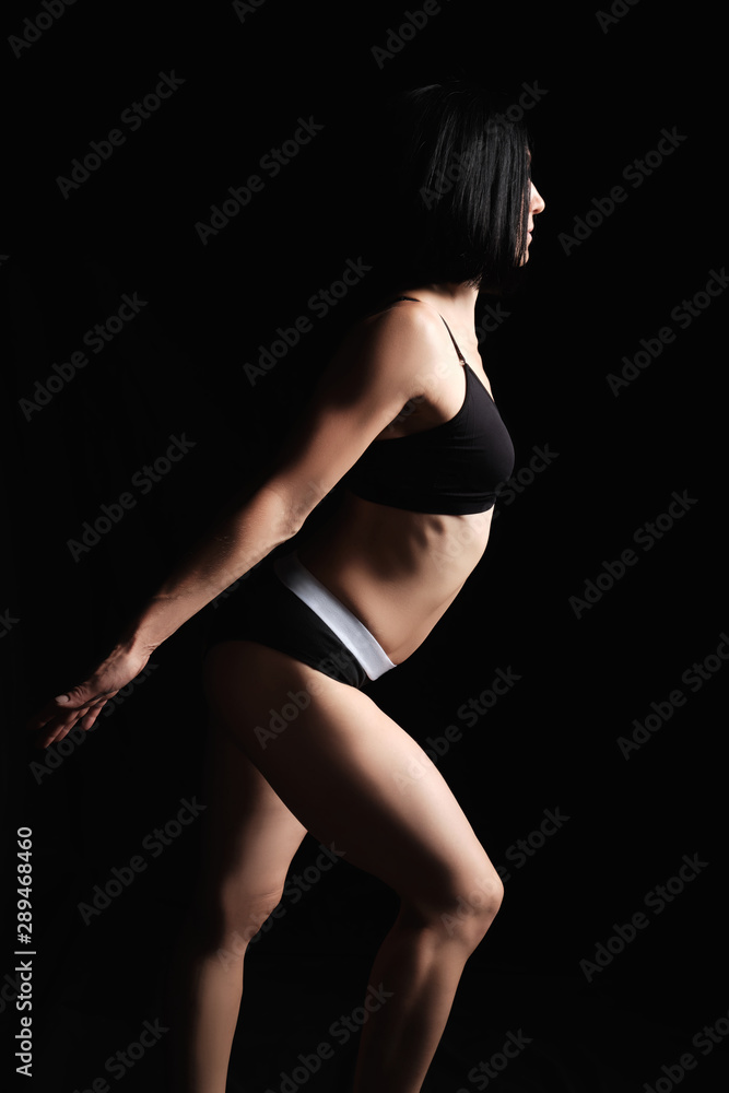 woman with a muscular body is dressed with a black topic and shorts stands sideways, the leg is set forward