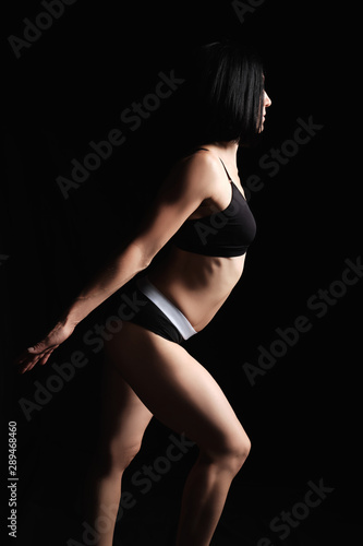 woman with a muscular body is dressed with a black topic and shorts stands sideways, the leg is set forward © nndanko