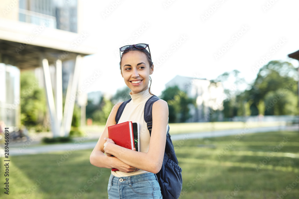 Portrait of smiling female student with a backpack and books going to college.