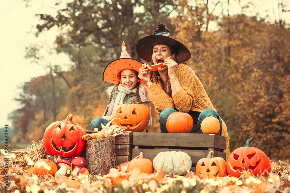 Fototapeta premium Mutter mit Tochter mit Hexenhut schnitzt Kürbis