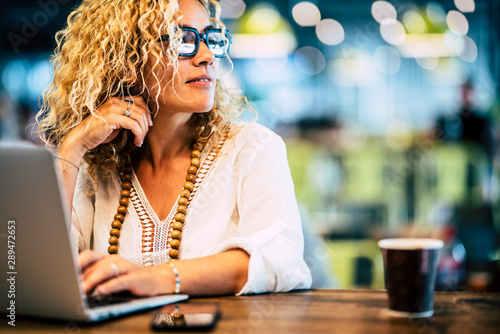 Beautiful adult caucasian people woman work at laptop computer with internet technology - concept of job and modern lady - phone and coffee on the table - defocused bokeh background photo