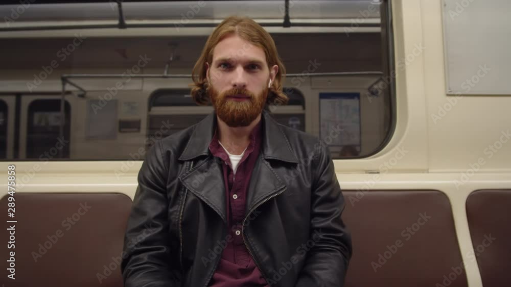 Low angle view of young handsome Caucasian man with red hair sitting in subway car and looking at camera Low angle view of young handsome Caucasian man with red hair sitting in subway car and looking at camera