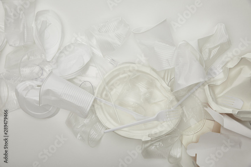 top view of crumpled plastic cups, plates and cardboard container on white background