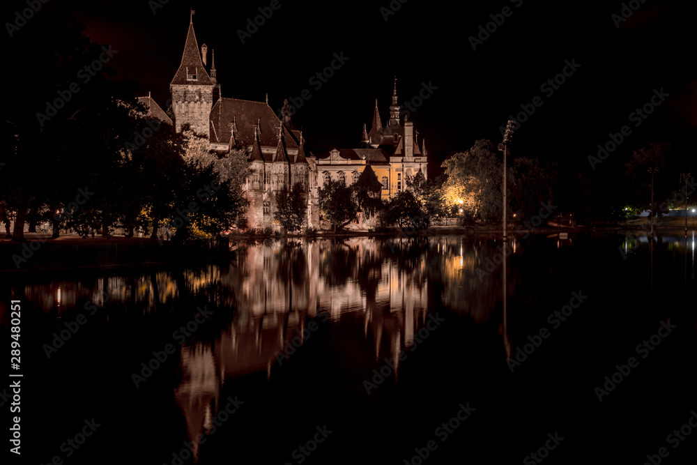 Night time view of lit Vajdahunyad castle in Varosliget with reflection on the lake in Budapest Hungary
