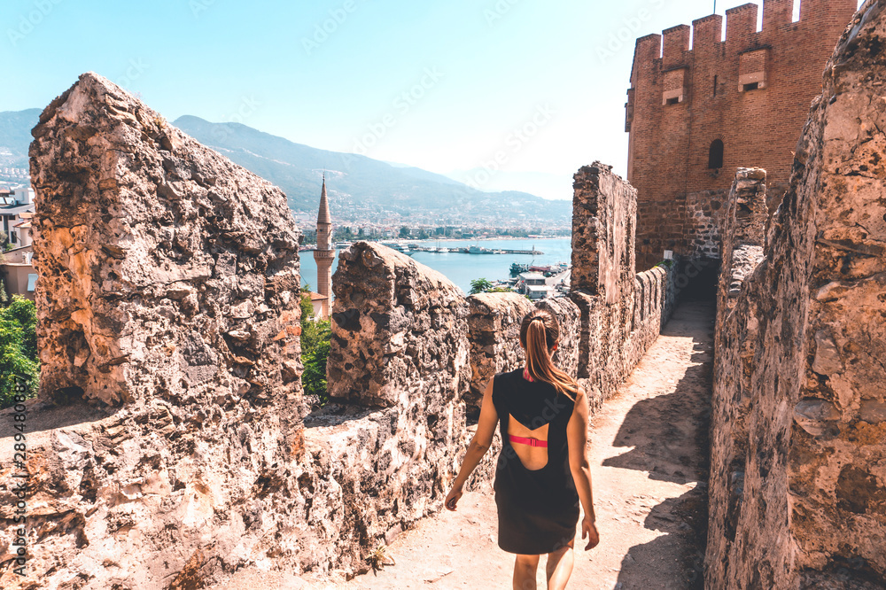 Naklejka premium Traveler exploring the city of Alanya in Turkey. Woman walking and discovering old landmark in Europe. Tourist sightseeing in the Red Tower. Travel lifestyle, wanderlust and freedom. Summer vacation.