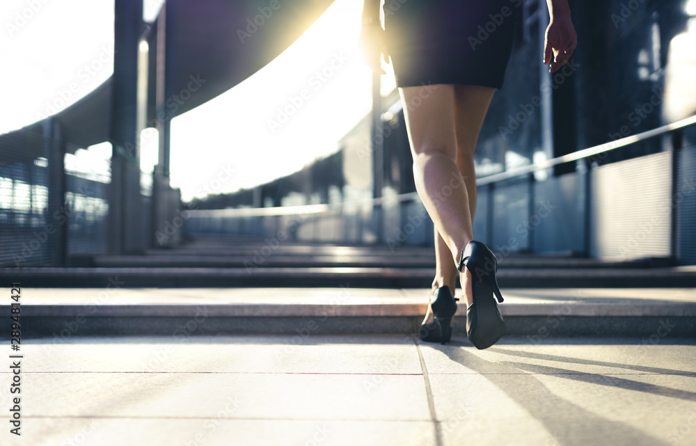 Business woman in high heels walking to work in city street in summer.  Elegant and stylish fashion lifestyle. Businesswoman or secretary in sexy  shoes. Happy professional lady. Career success. Stock Photo