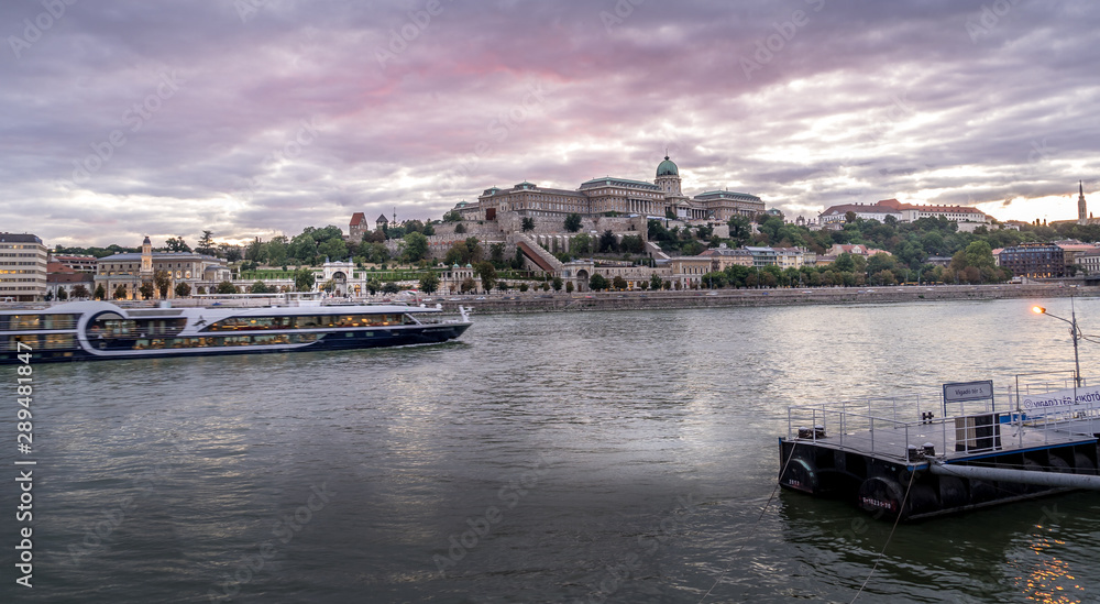 Buda castle with a river cruise passing by on the Danube with dramatic sunset sky in Budapest Hungary
