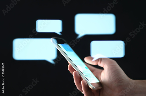 Text messages in cellphone screen with abstract hologram speech bubbles. Instant messaging app. Texting, group chat, sexting or sms concept. Customer service help desk with live support chatbot. photo
