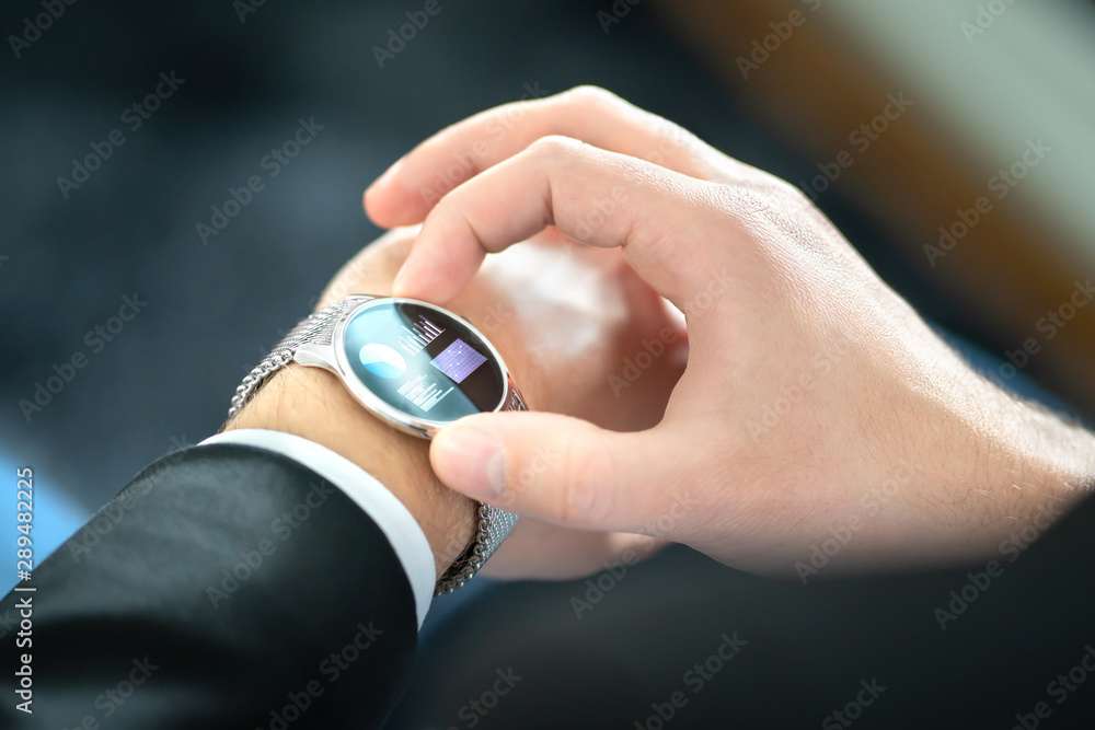 Fototapeta premium Smart watch with touch screen. Business man using wearable device with mobile technology. Smartwatch with finance report or banking app. Person wearing digital gadget in hand. Hybrid wearables concept