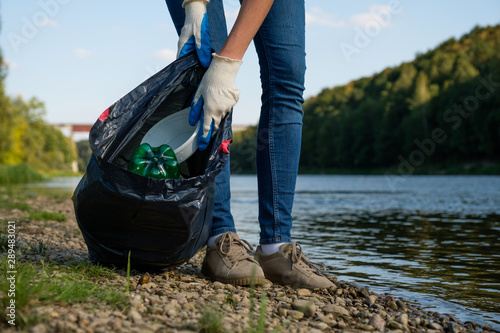 Volunteer woman collecting plastic rubbish on coast of the river. Cleaning environment concept