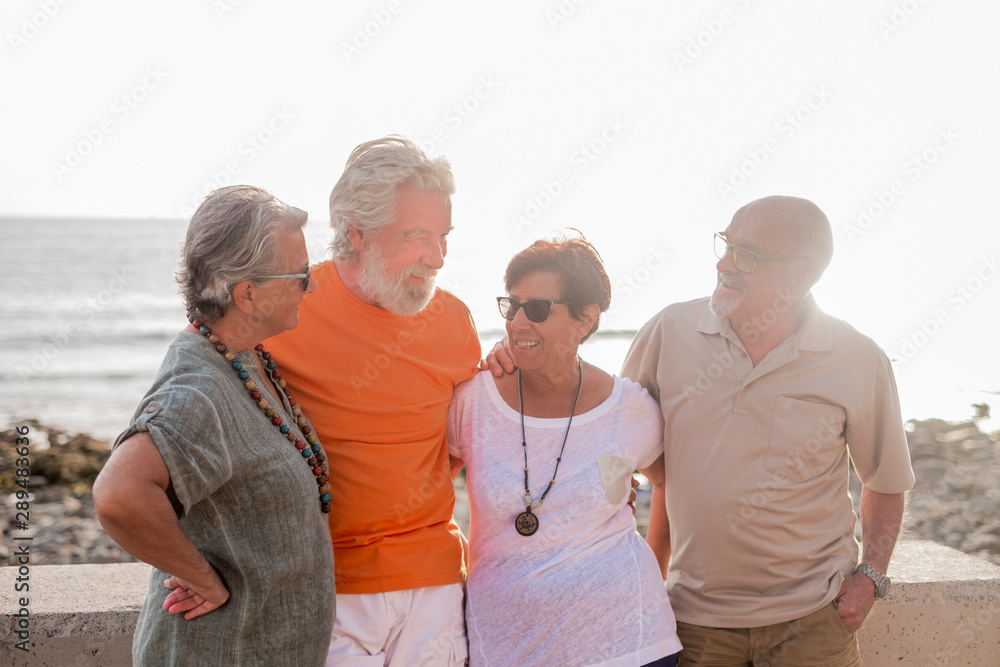 group of seniors and mature people at the beach taking together and having fun with the sea or the ocean at the background - four persons group of seniors and mature people at the beach taking together and having fun with the sea or the ocean at the background - four persons