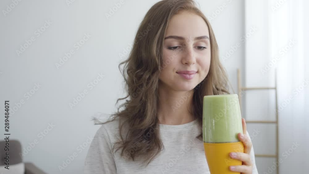 Portrait of young smiling woman making smoothie in the shaker in the kitchen at home. Concept of healthy food. Profession of nutri therapist, nutraceutical, nutritionist, wellness coach Portrait of young smiling woman making smoothie in the shaker in the kitchen at home. Concept of healthy food. Profession of nutri therapist, nutraceutical, nutritionist, wellness coach