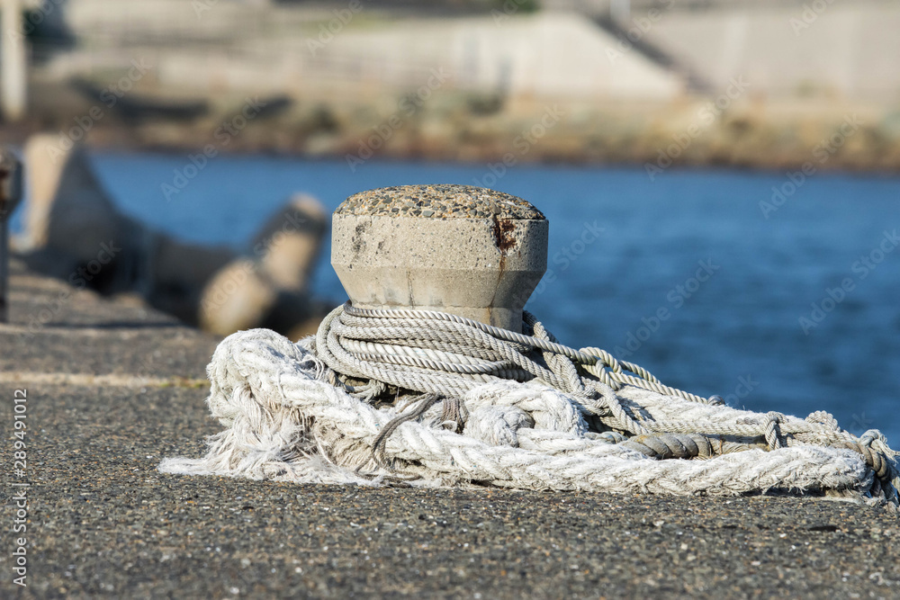 Fototapeta premium Concrete mooring bollard with a rope around it at a dock. 
