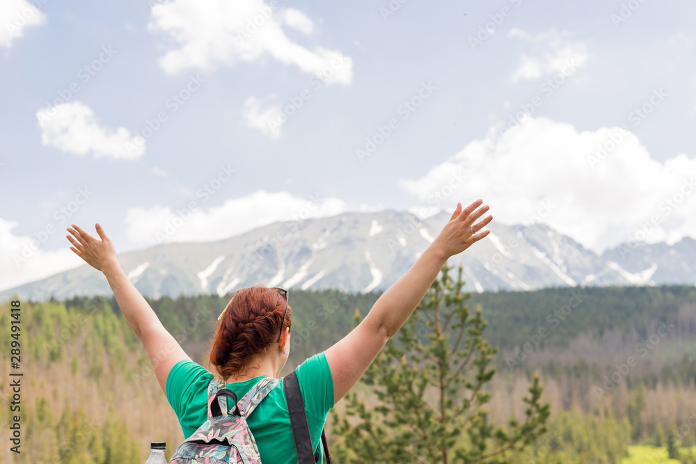 Successful young woman backpacker open arms on mountain peak. Pretty redheaded girl stands on spring snow mountains. Trekking and tourism concept. Copy space Successful young woman backpacker open arms on mountain peak. Pretty redheaded girl stands on spring snow mountains. Trekking and tourism concept. Copy space