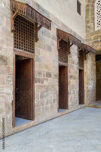 Facade of old abandoned stone bricks wall with three open weathered wooden doors and windows covered with wooden grid, Old Cairo, Egypt