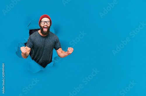 Young happy hipster guy looking through hole in paper. Crazy emotions. Copy space for your text or slogan. Discount, sale, season sales. Black friday. photo