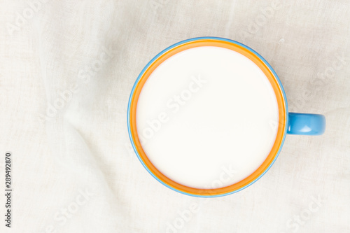 Top view of milk in blue and orange ceramic cup on white cloth background with copy space. 