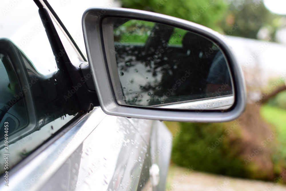 Fragment of a silver car with a side mirror. Raindrops on the mirror.