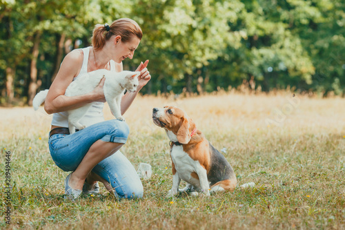 Pet owner kneeling hoding her cat and training her dog