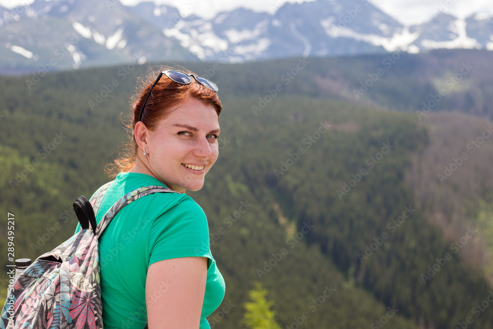 Woman traveler with backpack sits on top of a mountain and looking at camera, wanderlust travel concept, space for text, atmospheric epic moment