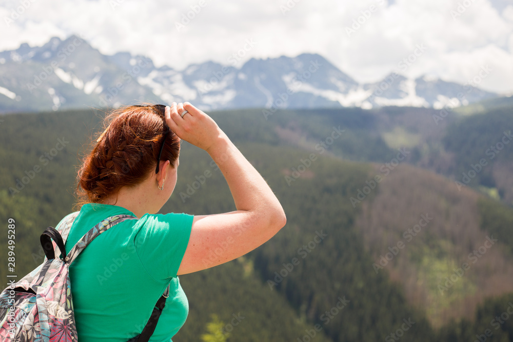 Woman traveler with backpack looking at amazing mountains and forest, wanderlust travel concept, space for text, atmospheric epic moment