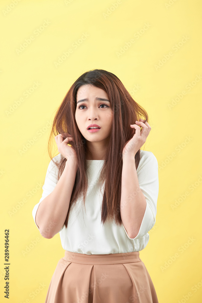 Portrait of woman confused damaged dry hair on yellow background Portrait of woman confused damaged dry hair on yellow background