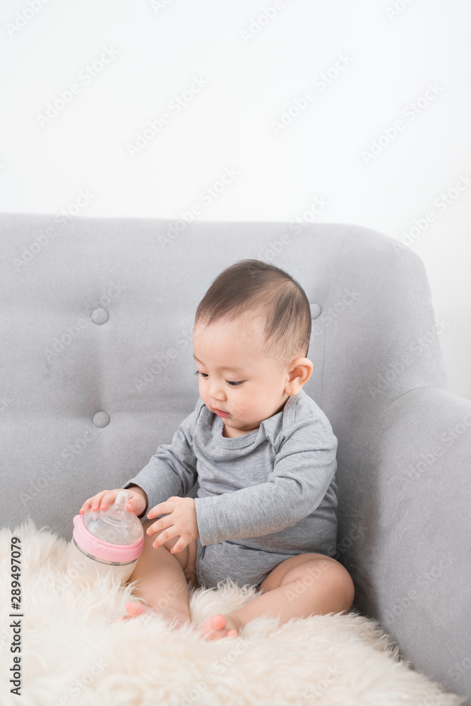 Little cute baby girl sitting in room on sofa drinking milk from bottle and smiling. Happy infant. Family people indoor Interior concepts. Childhood best time! Little cute baby girl sitting in room on sofa drinking milk from bottle and smiling. Happy infant. Family people indoor Interior concepts. Childhood best time!