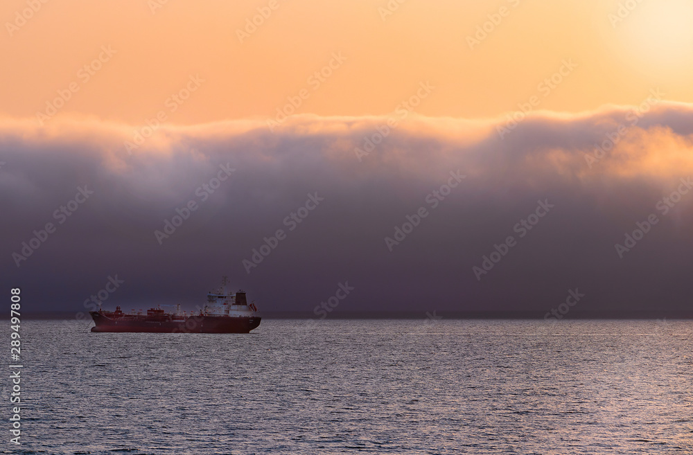 Heavy vessel on the horizon under dramatic clouds and bright sky. Beautiful African sunset. 