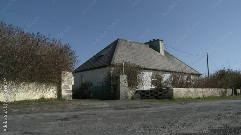 A grey house with a tall, steep roof and a low concrete wall out front, seen from across the street A grey house with a tall, steep roof and a low concrete wall out front, seen from across the street