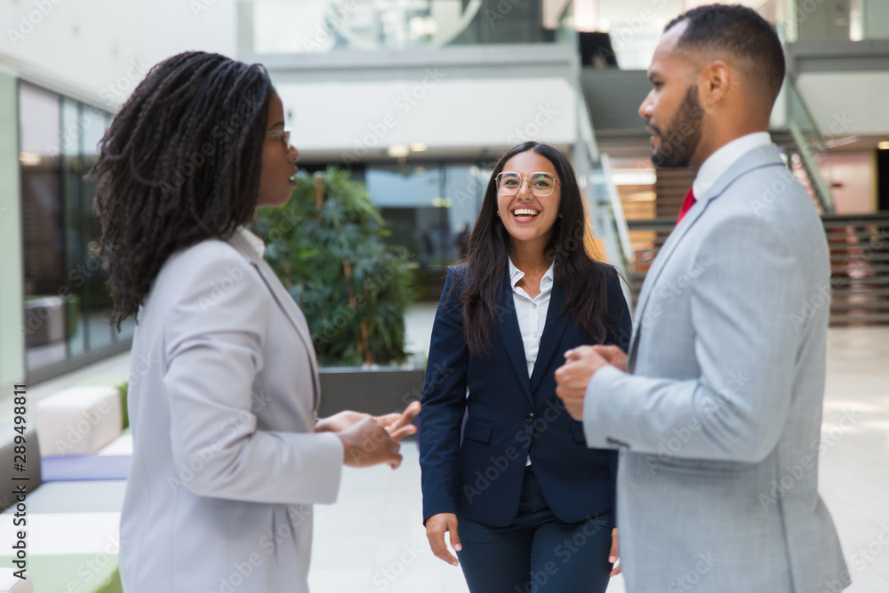 Happy confident businesswoman welcoming partners in office hall. Young business woman smiling and walking to diverse business couple. Meeting concept Happy confident businesswoman welcoming partners in office hall. Young business woman smiling and walking to diverse business couple. Meeting concept