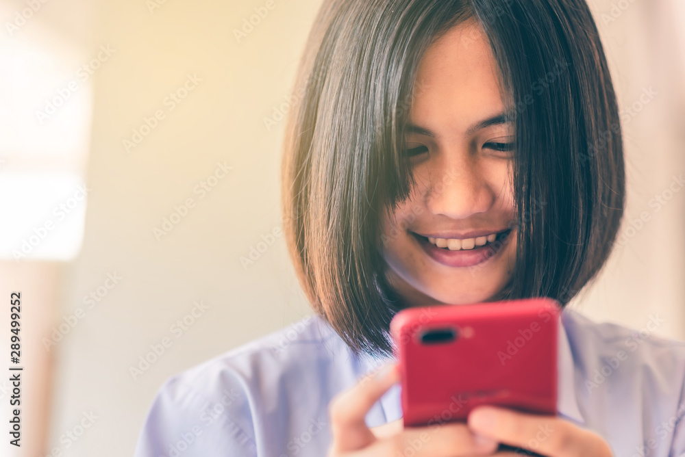 Smiling female Asian high school student in white uniform is enjoying social media on her smartphone. Smiling female Asian high school student in white uniform is enjoying social media on her smartphone.