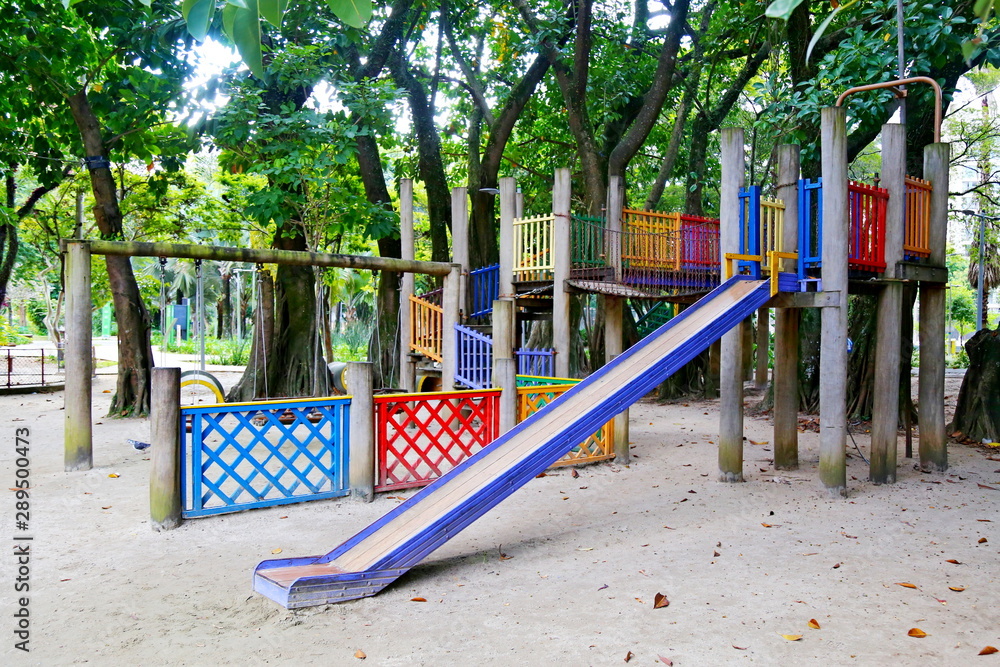 Playground surrounded by a park, with blue, red and yellow equipment