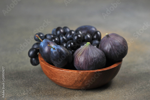 Figs, plums and grapes in a wooden bowl. The concept of purple fruits. Dark background. Close-up. Free space for text.