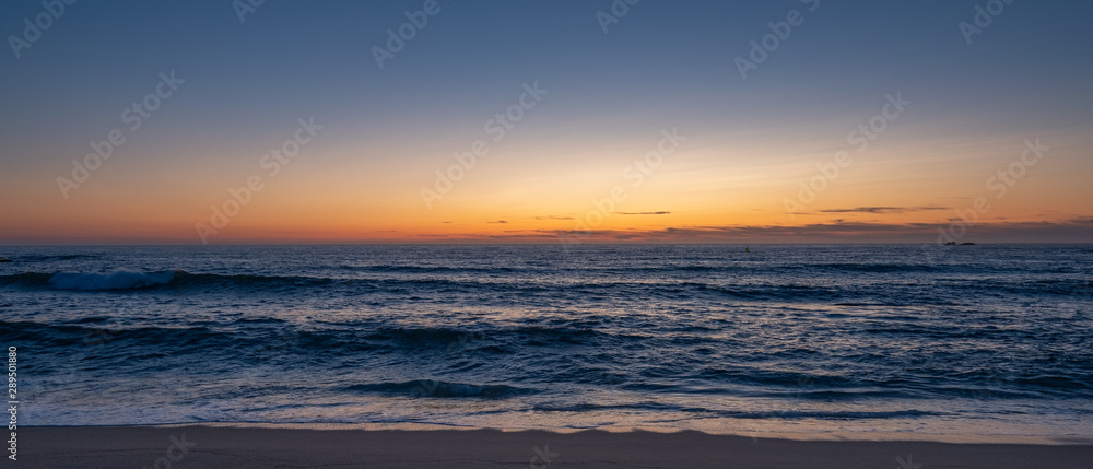 Wide shot over beach at dusk, parallel to shoreline with blue orange gradient sky