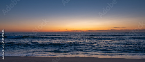 Wide shot over beach at dusk  parallel to shoreline with blue orange gradient sky